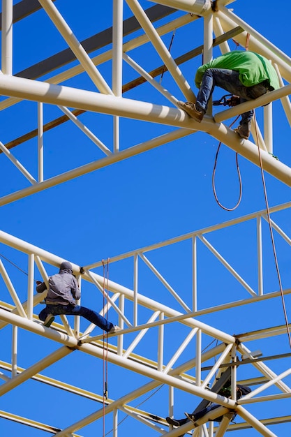 Aziatische bouwvakkers groeperen metaal op dakconstructie tegen blauwe lucht