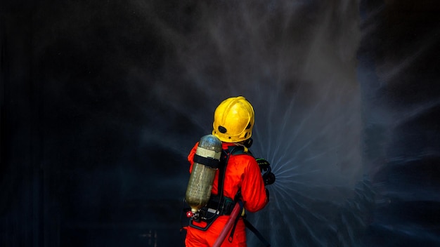 Aziatische brandweerman dienstdoende brandbestrijding Aziatische brandweerman spuit water onder hoge druk Brandweerman in brandblusapparatuur uniform spuitwater uit slang voor brandbestrijding