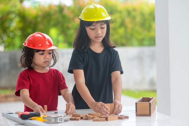 Aziatische broers en zussen die technische hoeden dragen, bouwen een huis van het houten speelgoed.