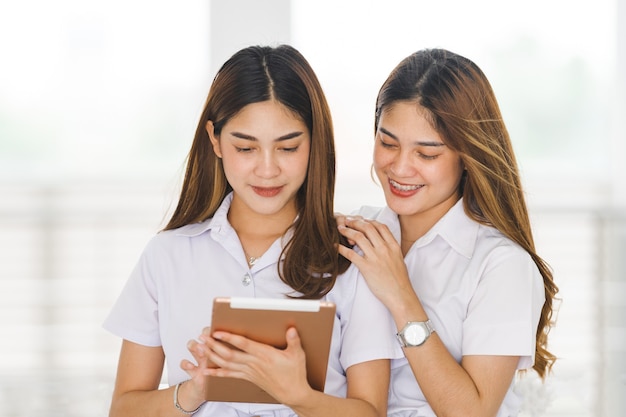 Aziatische broers en zussen in studentenuniform die interactie hebben en naar een digitale tablet kijken om samen te studeren op de universiteitscampus. Onderwijs stockfoto's