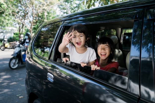Aziatische broers en zussen zwaaien met de handen uit het raam en reizen met de auto