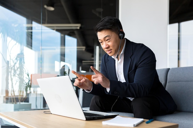 Aziatische callcentermedewerker praat met klanten die op kantoor zitten Aziatische zakenman die headset en laptop gebruikt voor videogesprekken, blij en glimlachend