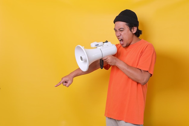 Aziatische casual man geïsoleerd op een gele achtergrond die door een megafoon schreeuwt en met de vinger naar beneden wijst