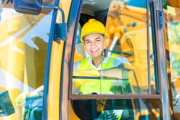 Aziatische chauffeur zit in de cockpit van bouwmachines van de bouwplaats