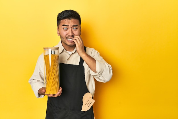 Aziatische chef-kok met spaghetti pot gele studio achtergrond bijten nagels nerveus en erg angstig