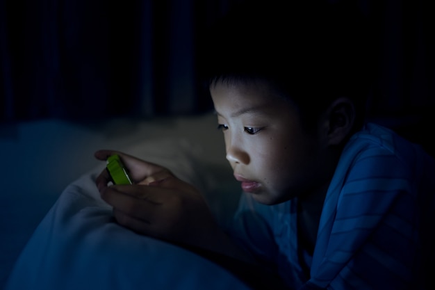 Aziatische Chinese jongen die smartphone op bed met lawaai en zachte nadruk speelt