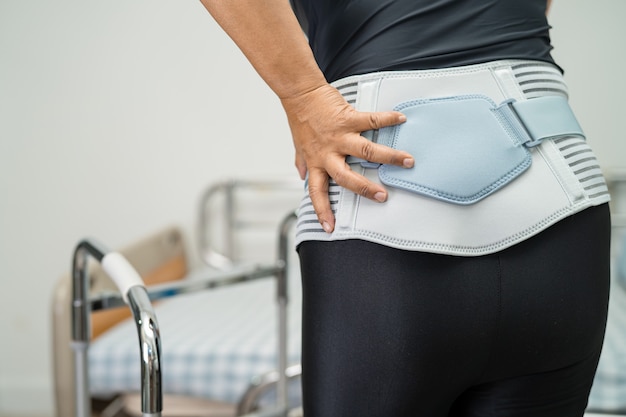 Aziatische damepatiënt die steunriem voor rugpijn draagt voor orthopedische lumbale met rollator.