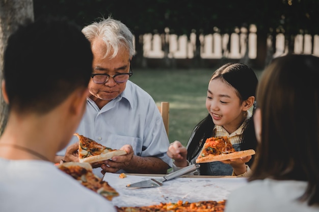 Aziatische familie die pizza in tuin heeft thuis. Ouder met kind en grootvader levensstijl in achtertuin.