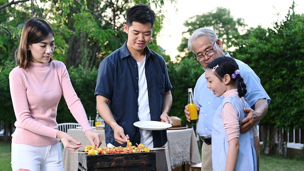 Aziatische familie met een barbecuefeestje thuis. Gegrilde bbq koken voor het diner in de achtertuin. Levensstijl op zomervakantie.