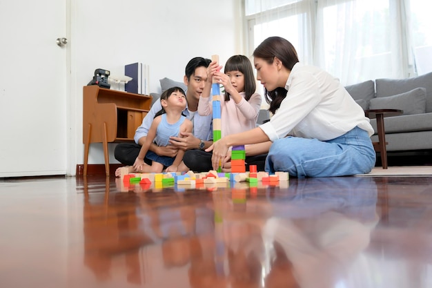 Aziatische familie met kinderen die spelen en een toren bouwen van kleurrijke houten speelgoedblokken in de woonkamer