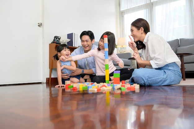 Aziatische familie met kinderen die spelen en een toren bouwen van kleurrijke houten speelgoedblokken in de woonkamer