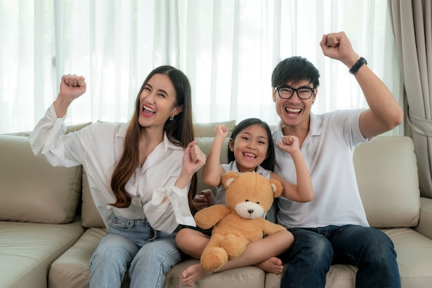 Aziatische familie met vader, moeder en dochter zitten en tv kijken en glimlachen