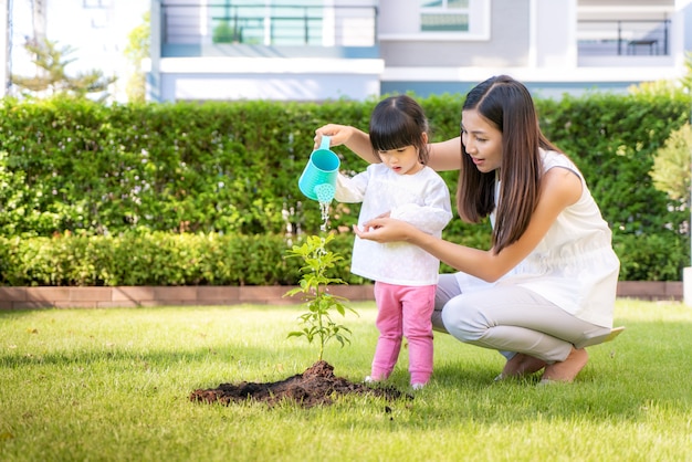 Aziatische familie moeder en kind dochter plant jonge boom en buiten water geven in de natuur lente voor het verminderen van de opwarming van de aarde groei functie en zorg aard aarde.