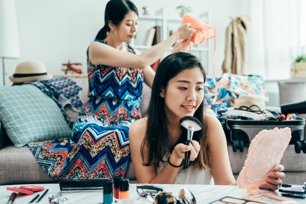 Aziatische familiereisconcept gelukszussen die spullen inpakken en plannen voor een vakantiereis met opgewonden en vrolijk. jong meisje zittend op de bank bank voorbereiden bagage. dame die 's ochtends make-up aanbrengt