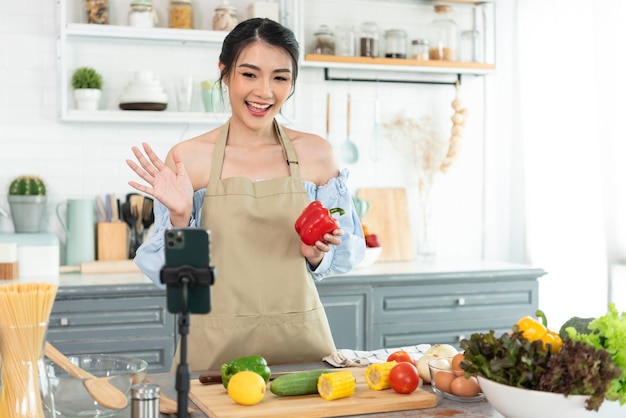 Aziatische foodblogger kookt salade voor de camera van een smartphone terwijl hij vlog-video opneemt en live streamt thuis in de keuken