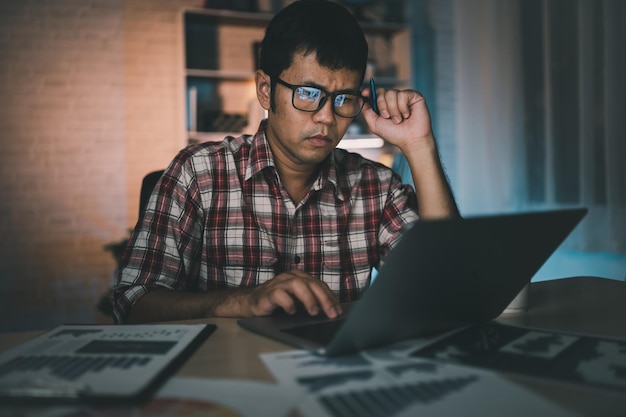 Aziatische freelance man met stressvolle depressie trieste tijd werken op laptop thuis nacht Depressie man triest serios werken vanuit huis Man met geruit overhemd rood haast zich overuren voor deadline