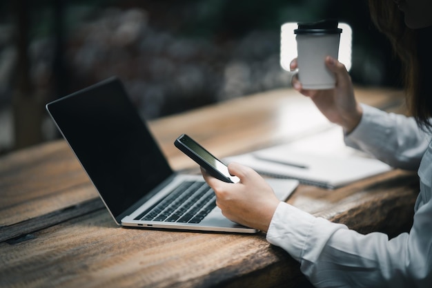 Aziatische freelance vrouw die lacht met kop warme koffie en werken op laptopcomputer op houten tafel in café ondernemersvrouw die voor haar bedrijf in coffeeshop werkt zakelijk werk van overal