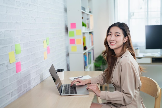 Aziatische freelance vrouw die lacht typen op toetsenbord en werken op laptop op houten tafel thuis Ondernemersvrouw die voor haar bedrijf in woonkamer thuis werkt Zakelijk werk thuis concept