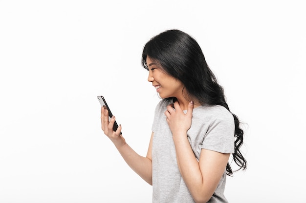 Aziatische gelukkig mooie jonge vrouw poseren geïsoleerd over witte muur met behulp van mobiele telefoon.