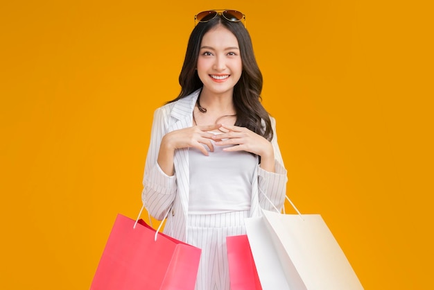 Aziatische gelukkig vrouwelijke vrouw meisje houdt kleurrijke winkelen pakketten permanent op gele achtergrond studio opname close-up portret jonge mooi aantrekkelijk meisje glimlachend camera kijken met zakken