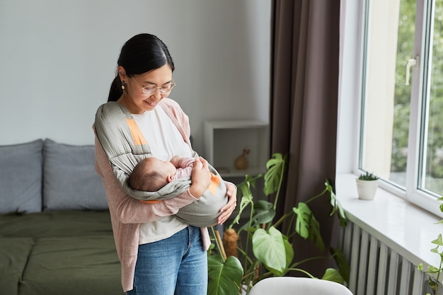 Aziatische gelukkige moeder houdt haar baby vast en wiegt haar terwijl ze door de kamer loopt