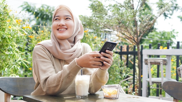 Aziatische hijab vrouw speelt telefoon in café