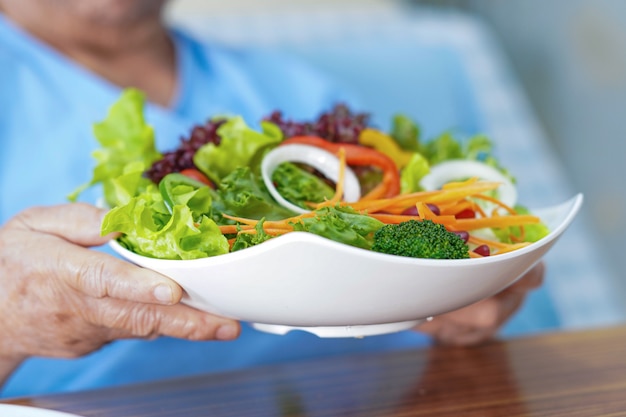 Aziatische hogere vrouw die salade plantaardig voedsel in het ziekenhuis eet