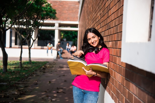 Aziatische Indiase student in focus die op laptop werkt of een boek leest terwijl andere klasgenoten op de achtergrond, buitenfoto op de universiteitscampus