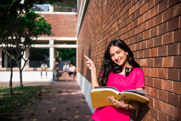 Aziatische Indiase student in focus die op laptop werkt of een boek leest terwijl andere klasgenoten op de achtergrond, buitenfoto op de universiteitscampus