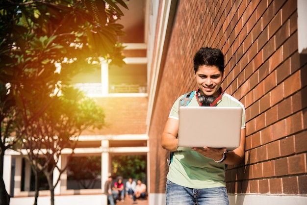 Aziatische Indiase student in focus die op laptop werkt of een boek leest terwijl andere klasgenoten op de achtergrond, buitenfoto op de universiteitscampus