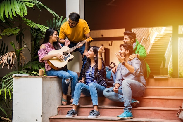 Aziatische Indiase studenten die muziek spelen met gitaar terwijl ze op de campus op trappen of over gazon zitten