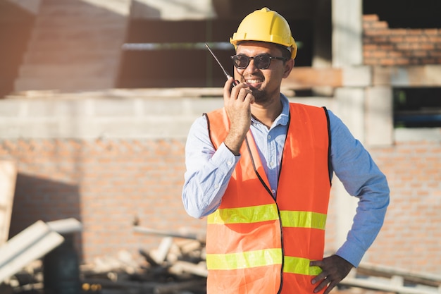 Aziatische ingenieur die radio gebruiken om team in bouwconstructie te belasten.