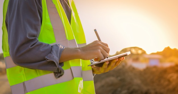 Aziatische ingenieur met bouwvakker die de computer van tabletpc het inspecteren en het werken gebruiken