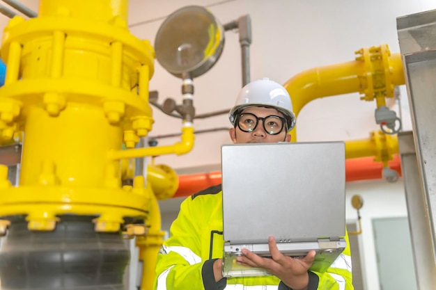 Foto aziatische ingenieur met een bril die in de stookruimte werkt, onderhoud controleert technische gegevens van hea