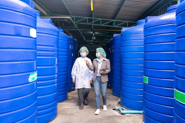Aziatische inspecteur supervisor vrouw en assistent-werknemer met gezichtsmasker om de voorraad watertank in de opslagruimte van de verwerkingsfabriek te controleren