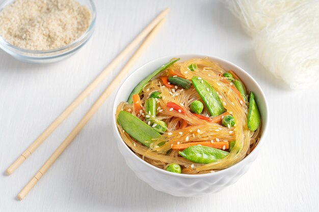 Aziatische Japchae-schotel van geroerbakte cellofaannoedels, groene erwten en bonen met eetstokjes op tafel