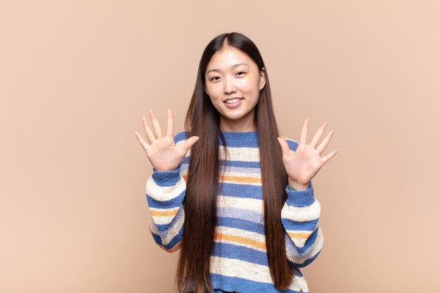 Aziatische jonge en vrouw die vriendelijk glimlacht kijkt, nummer tien of tiende met vooruit hand toont, aftellend