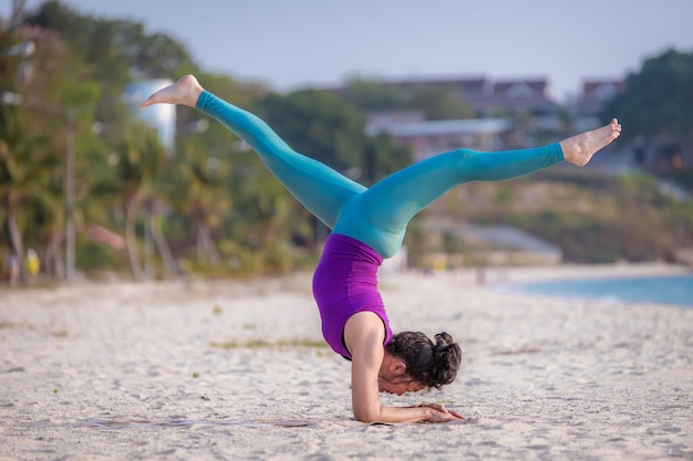 Aziatische jonge gezonde vrouw poseren paradijsvogel yoga op stenen strand met blauwe wolkenlucht