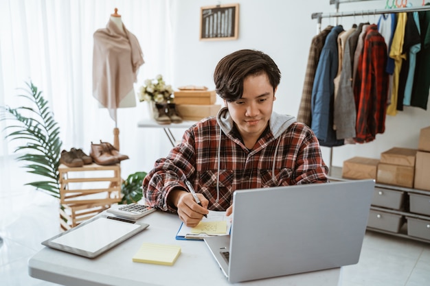 Aziatische jonge man aan het werk op een laptop in een kledingwinkel