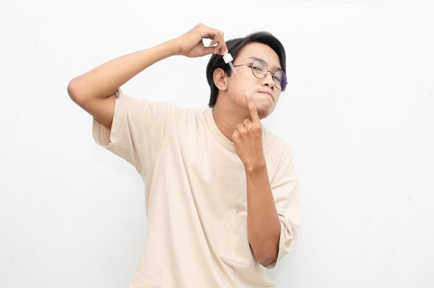 aziatische jonge man in casual beige t-shirt die schoonheidsacne-serum aanbrengt met behulp van een pipet