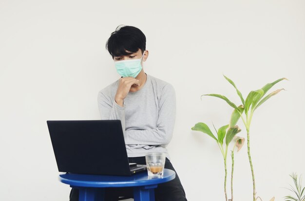 Aziatische jonge man met een masker die voor een laptop zit die bezig is met zijn werk