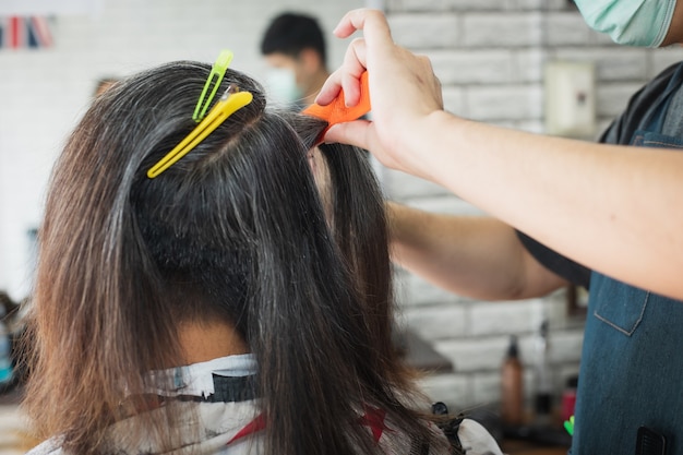 Aziatische jonge man wordt gesneden uit lang haar tot kort haar met een schaar door professionele kapper in de kapsalon.