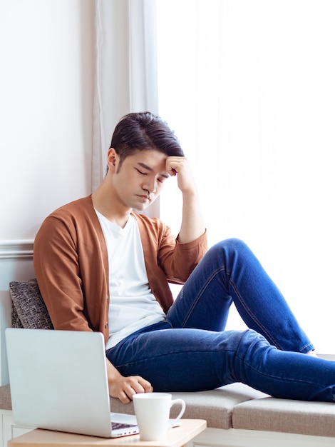 Aziatische jonge man zit aan de tafel voor een laptopcomputer