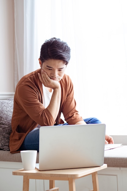 Aziatische jonge man zit aan de tafel voor een laptopcomputer