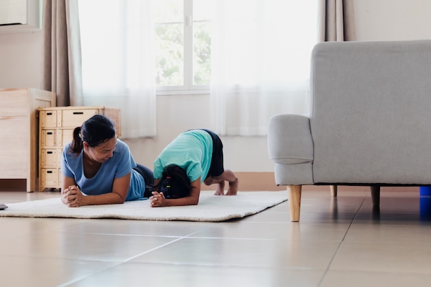 Aziatische jonge moeder en haar dochter doen stretching fitness yoga samen thuis. ouders die het kind leren, werken om sterk te zijn en de fysieke gezondheid en het welzijn in de dagelijkse routine te behouden.