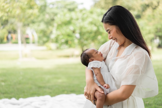 Aziatische jonge mooie moeder die haar pasgeboren baby vasthoudt, slaapt en voelt met liefde en raakt zachtjes aan en zit dan op groen gras in het park