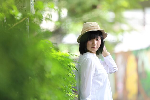 Aziatische jonge vrouw die denkt en het portret van het reisconcept met groene boomachtergrond denkt
