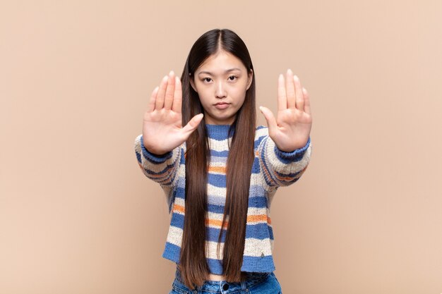 Aziatische jonge vrouw die ernstig, ongelukkig, boos en ontevreden kijkt en toegang verbiedt of stop zegt met beide open handpalmen