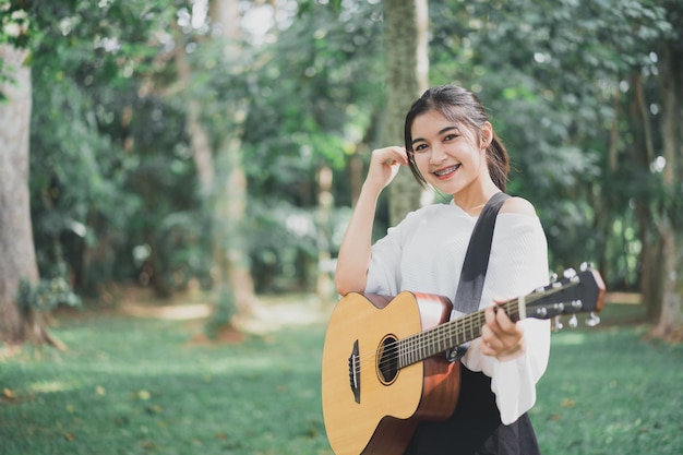 Aziatische jonge vrouw die gitaar speelt en muziek zingt in het park Aziatische vrouw die gitaar speelt in de tuin