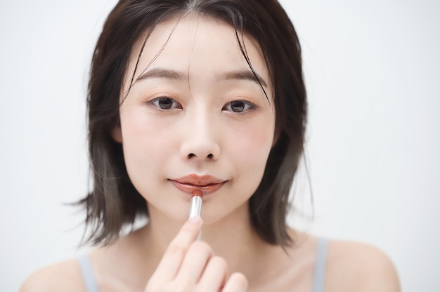 Aziatische jonge vrouw die lippenstift op haar lippen aanbrengt